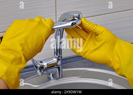 Kitchen faucet repair. A worker in yellow rubber gloves uses an adjustable wrench to unscrew the aerator Stock Photo