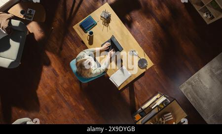 Top View of Home Office: Freelance Entrepreneur Sitting at Desk, Using Laptop. Female Professional Works from Home, Manages Company Remotely, Designs Software. Remote Access Work Concept. Stock Photo