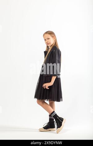 A full-length portrait of a young girl with long brown hair dressed in a hooligan style on white background in studio. Stock Photo