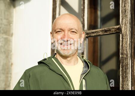 Senior Man Smiling in Sunlit Urban Environment Wearing Green Jacket Stock Photo