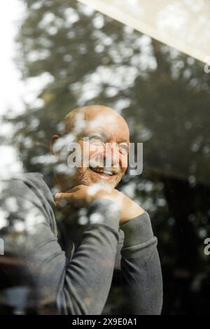 Elderly man smiling with hands on chin behind a reflective window Stock Photo