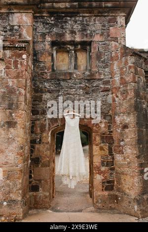 Bride's lace dress hangs on castle wall Stock Photo