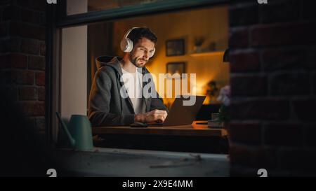 Professional Software Engineer Working From Home Office. Tired IT Specialist Feeling Sleepy and Finising Important Project. Application Development Process. View From Outdoors into Window. Stock Photo
