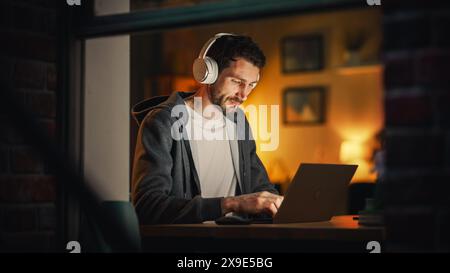 Professional Software Engineer Working From Stylish Home Office. Tired IT Specialist Feeling Sleepy and Finising Important Project. Application Development Process. View From Outdoors into Window. Stock Photo
