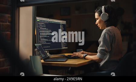 Brazilian Female Programmer Working on Computer at Home. Brilliant Female IT Programer Using Desktop Computer Late Night. Professional Developer Programming Code. Shot Into the Window From Outside. Stock Photo