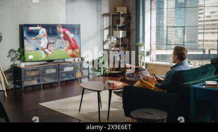 Sports Fan Watches Important Soccer Match on TV at Home, He Aggressively Gestures with the Fist, Cheering for His Team. His Successful Team Scores a Goal and He Celebrates the Win. Stock Photo