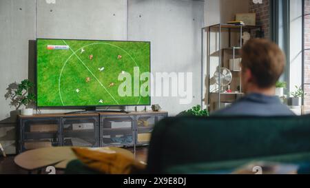 Sports Fan Watches Important Soccer Match on TV at Home, He Is Focused on Intense Championship Finals, Cheering for His Team. His Successful Team Scores and Leading the Game. Stock Photo