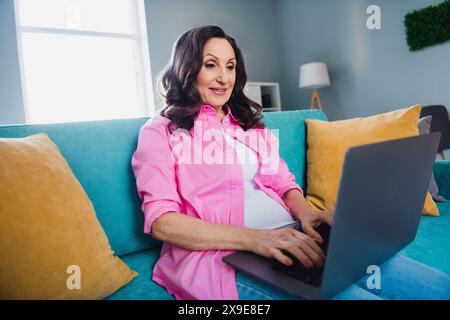 Photo of lovely pretty retired woman sitting sofa working from home using netbook indoors Stock Photo