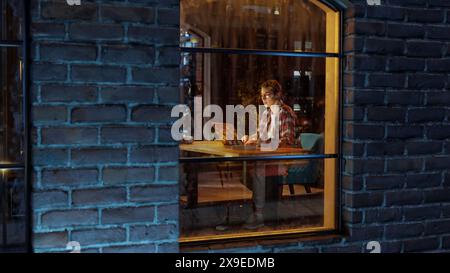 Female Specialist Working on Laptop Computer in Stylish Apartment. Creative Professional Managing Corporate Social Media, Browsing Internet. Freelancer Remotely Works From Home. View Through Window. Stock Photo