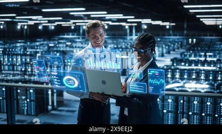Technical Engineer and Project Administrator Using Computer in Modern Data Center Server Room Facility. Augmented Reality Productivity and Business Data Icons Appear From Worker's Laptop. Stock Photo