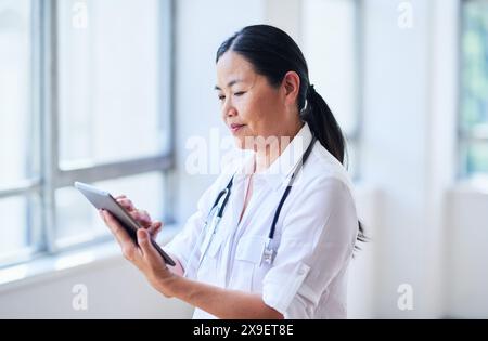 Focused Female Doctor Using Digital Tablet in Bright Hospital Corridor Stock Photo