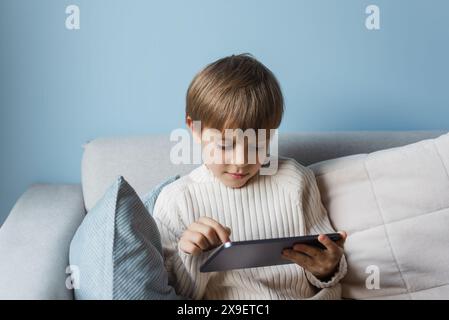 Boy is relaxing on the sofa at home and using a tablet. Stock Photo