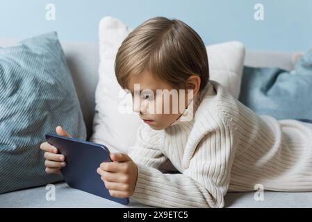 Boy is relaxing on the sofa at home and using a digital tablet. Stock Photo
