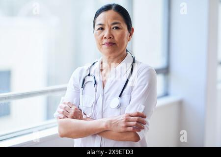 Confident Female Doctor Standing with Arms Crossed in Hospital Corridor Stock Photo