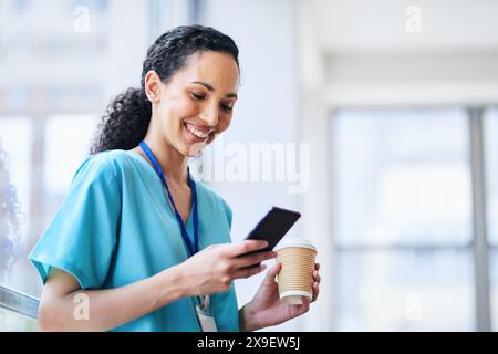 Smiling Female Doctor in Hospital Scrubs Using Smartphone with Coffee Stock Photo