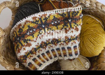 Close-up photo of Fair Isle wool knitted hat in progress on the needles with yarn balls in a wicker basket Stock Photo