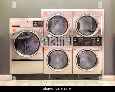 Industrial laundry dryers with digital control panels in a self-service laundromat, aligned and numbered. Stock Photo