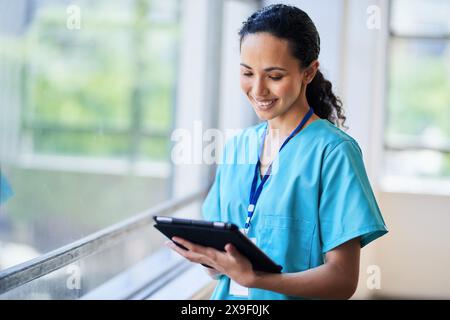 Smiling Nurse in Hospital Scrubs Using Digital Tablet in Modern Medical Facility Stock Photo