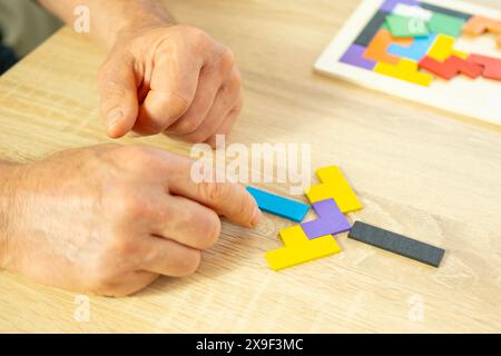 male hand manipulates colorful wooden puzzle, elderly old man composing geometric shapes, brain health and mental well-being, preventing dementia and Stock Photo