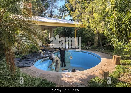 Workman using rollers and a paintbrush to apply fibreglass gel coat paint to an old swimming pool. Stock Photo