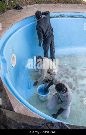 Workman using rollers and a paintbrush to apply fibreglass gel coat paint to an old swimming pool. Stock Photo