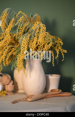 Vase of mimosa flowers on a table with wooden spoons and egg cups Stock Photo