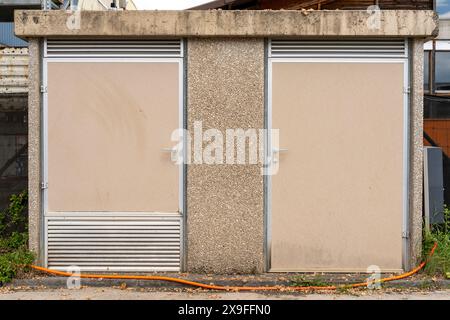 Transformer house with two locked doors and little electriciy warning signs. Big orange cable running in front of that station. Stock Photo