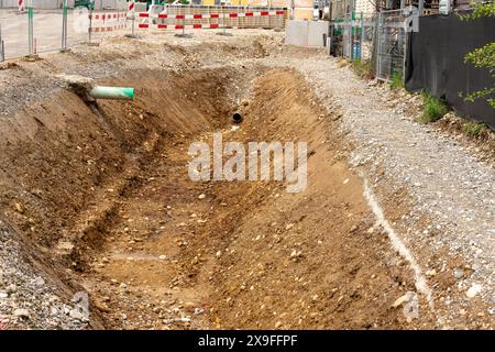 Excavator hole with pipes protruding into the hole from two sides. Texture with eartg, clay and pebbles in the hole. Red white barrier at one end of t Stock Photo