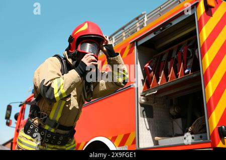 Firefighter in uniform wearing helmet and mask near fire truck outdoors, low angle view Stock Photo