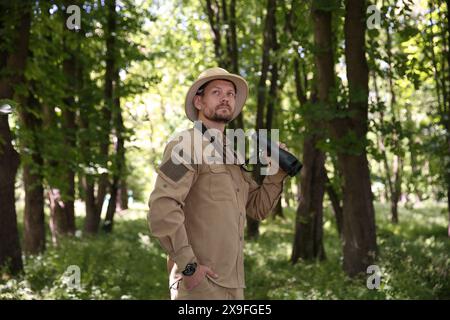 Forester with binoculars examining plants in forest Stock Photo