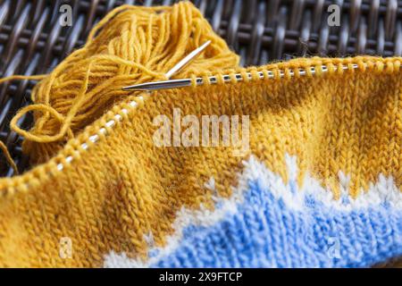 Yellow blue white wool yarn knitting on the metal needles, stockinette stitch knitted texture in progress close-up photo Stock Photo