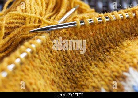 Close-up photography of a yellow icelandic wool yarn knitting on the metal needles with yarn ball, stockinette stitch knitted texture in progress Stock Photo