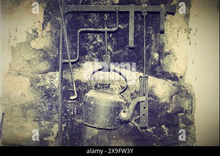 An old kettle on a hook, hanging over the hearth. Old photo. Stock Photo