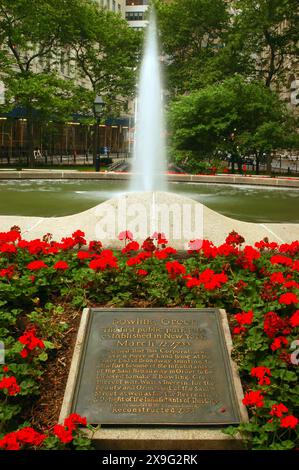 A plaque in a flower garden, near a gushing water fountain notes Bowling Green was the first public park in New York City Stock Photo