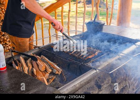 Man cooking some salmon fillets on a stone barbecue outside the Historic Taku Glacier Lodge, a wooden cabin located in the mountains north of the Alas Stock Photo