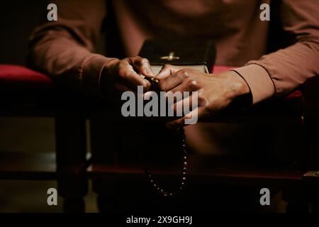 Hands of unrecognizable Black man holding rosary praying in Catholic church, copy space Stock Photo