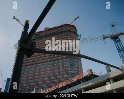 View up with street pole foreground to multi-story parking garage, building and cranes under construction. Blue sky and orange fencing. No people Stock Photo