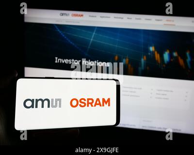 Person holding smartphone with logo of Austrian electronics company ams OSRAM AG in front of website. Focus on phone display. Stock Photo