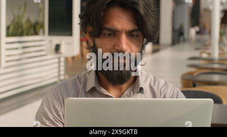 Concentrated serious indian man busy focused businessman office worker manager employee typing laptop working online with computer thinking problem Stock Photo