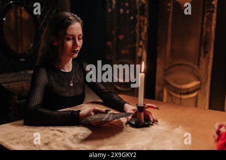 Portrait of mysterious fortuneteller shuffling tarot cards during magic ritual in dark room by light of burning candle. Enigmatic fortune teller tarot Stock Photo