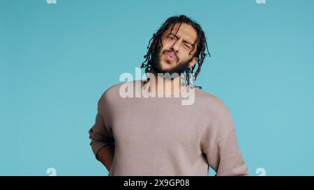Hurt Middle Eastern man screaming from pain, suffering from back injury, having health problems. Injured BIPOC person feeling uncomfortable ache, yelling, studio background, camera B Stock Photo