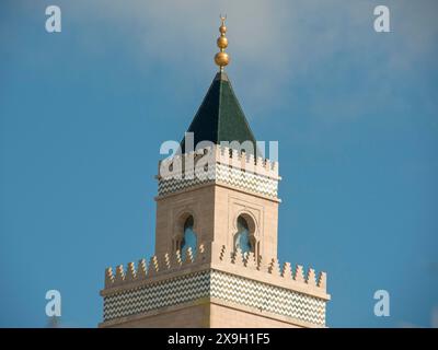 A tall minaret with a green spire and golden decorations rises into the sky, Tunis in Africa with ruins from Roman times, modern mosques and blue and Stock Photo