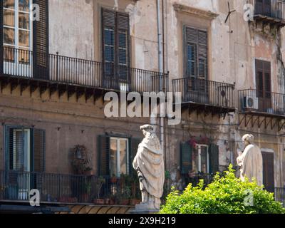 Two statues in front of an old building with balconies and shutters, decorated with green plants, palermo in sicily with an impressive cathedral Stock Photo