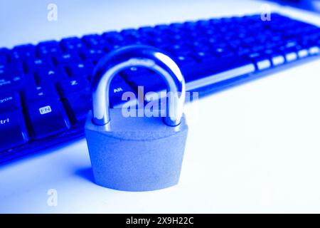 A closed padlock next to a computer keyboard on a white background with copy space, illuminated by a blue light. Stock Photo