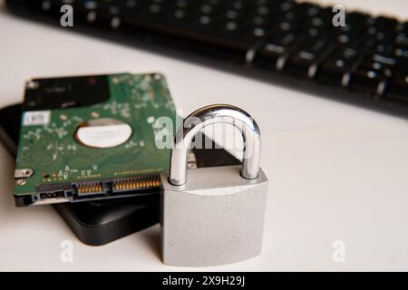 A closed padlock next to two hard disks, in the background a computer keyboard on a white background. Stock Photo