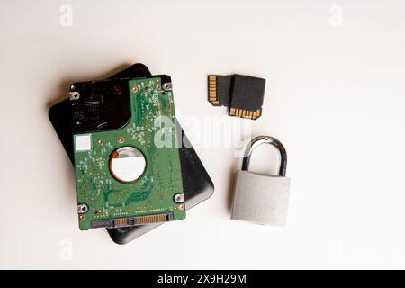 A closed padlock next to two hard disks, in the background a computer keyboard on a white background. Stock Photo