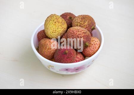 Fresh ripe lychees on a white bowl on light wooden surface. Its scientific name is Litchi chinensis. Stock Photo