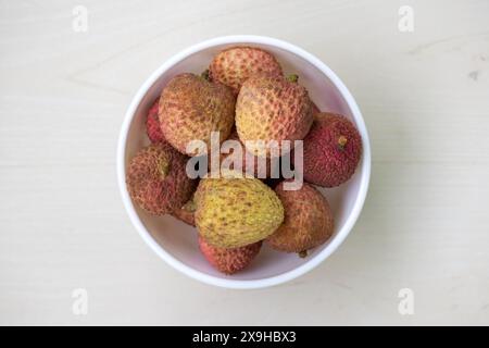 Fresh ripe lychees on a white bowl on light wooden surface. Its scientific name is Litchi chinensis. Stock Photo