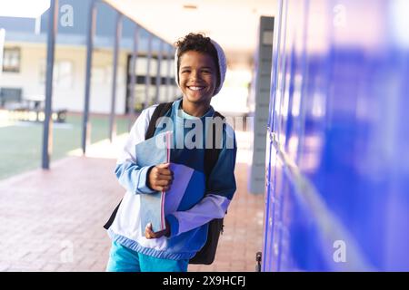 Biracial boy stands smiling on a sunny grass field, mountains in the ...