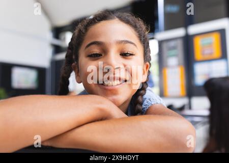 Biracial girl with braided hair smiles warmly, resting her chin on her arms Stock Photo